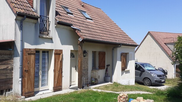 Ein zweistöckiges Haus mit Ziegeldach, Holzzaun und einem geparkten Auto.