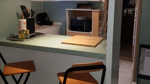 Eine kompakte Küche mit Mikrowelle, Toaster und Schneidebrett aus Holz auf der Arbeitsplatte. Zwei Hocker und ein Schrank mit Milchglasfronten sind ebenfalls vorhanden.