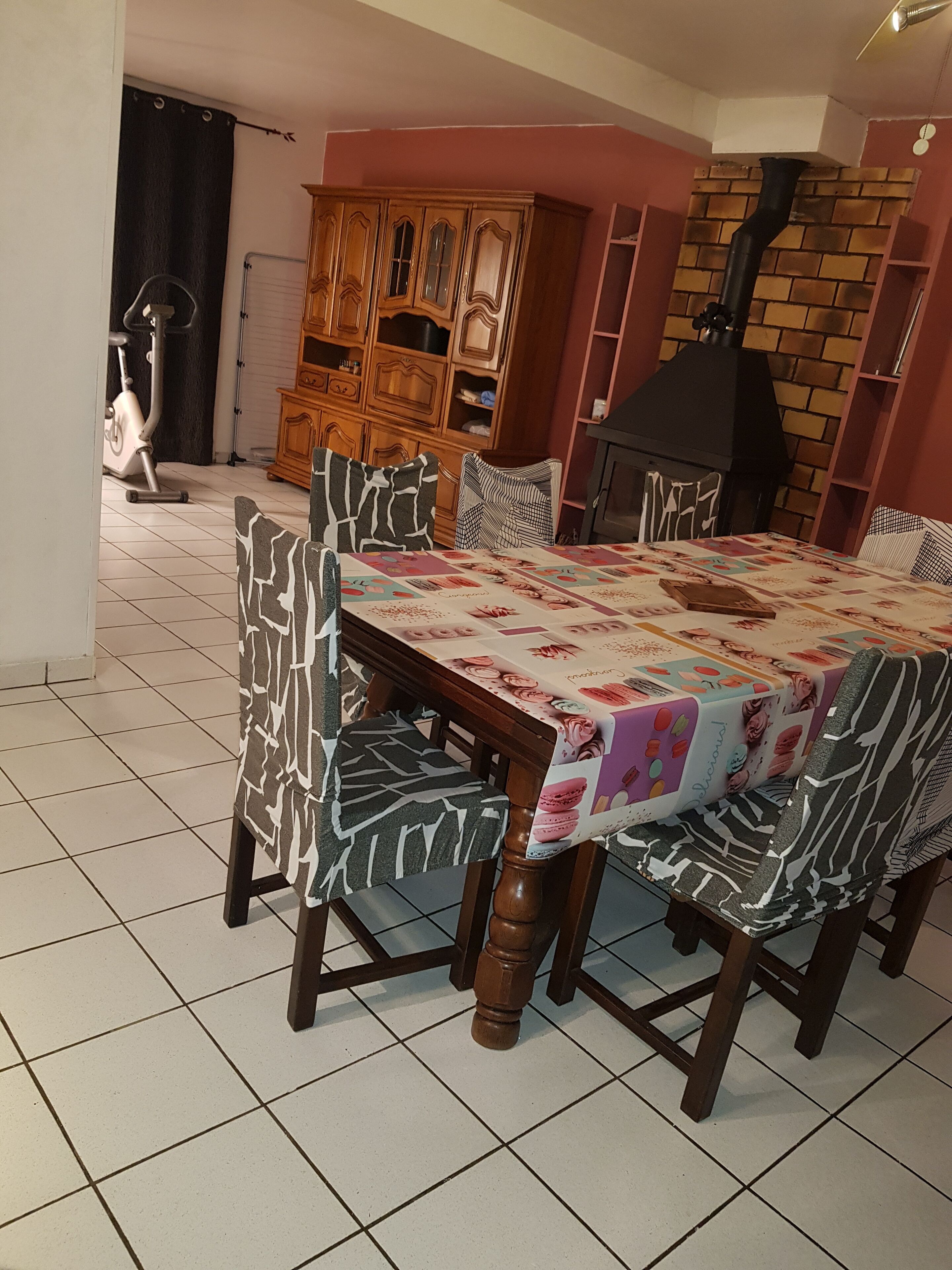 Un coin repas avec un sol carrelé, une table recouverte d’une nappe à motifs floraux et des chaises à motifs.