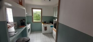 Eine kleine Küche mit Fenster, weißen Schränken und Fliesenboden.