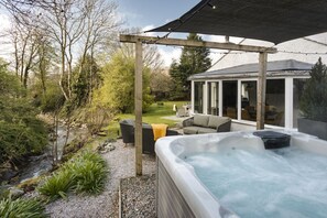 Ett bubbelbad med en pergola, utomhusmöbler och utsikt över ett hus med en glasdörr.