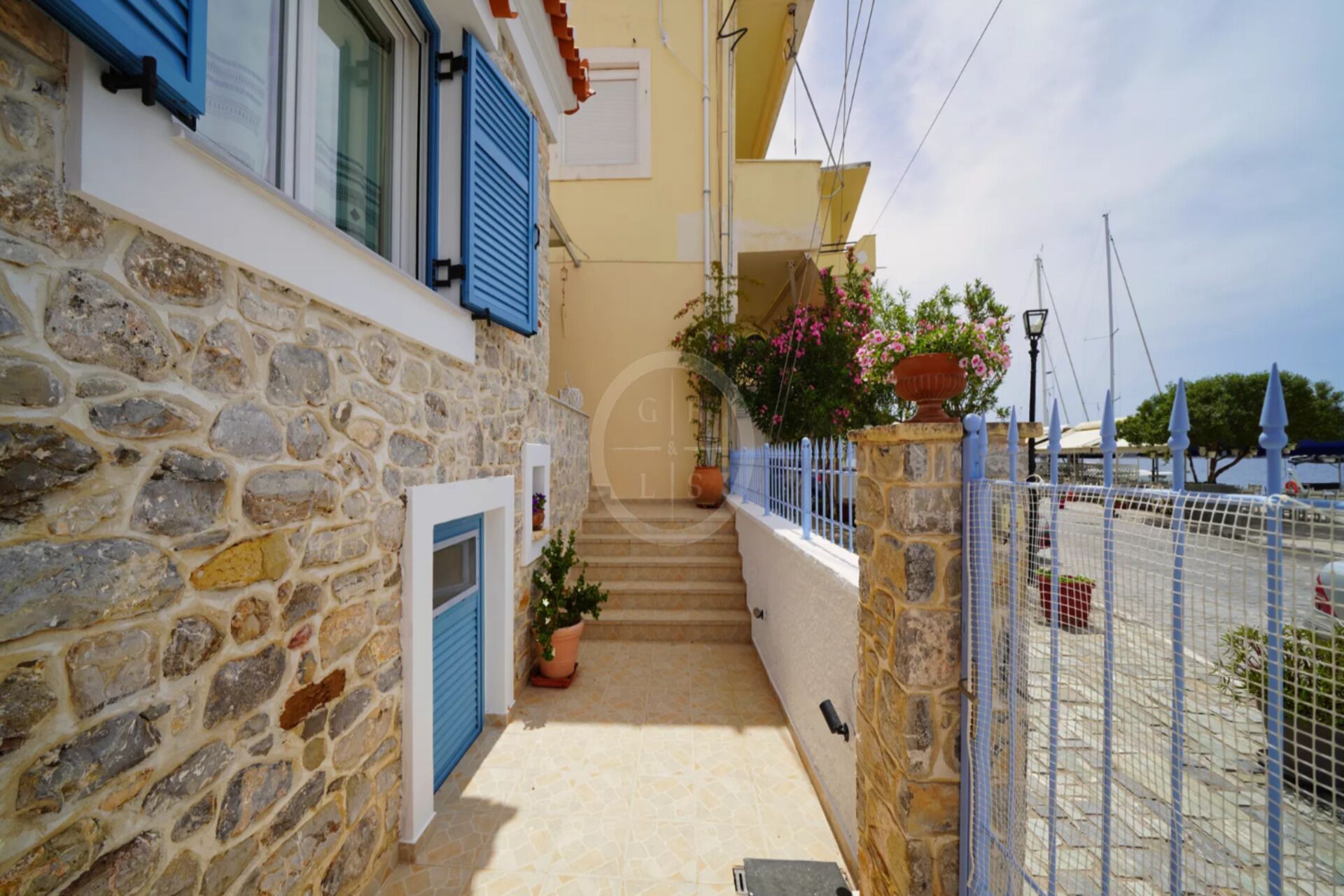 A stone building with blue shutters, a tiled entrance, and a metal fence.