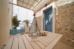 A wooden table with a sailboat model, a blue door, and a stone wall. - Elli Apartment in Ermioni (Ermioni)