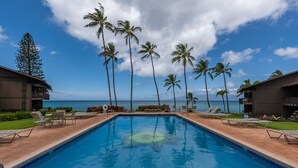 Una piscina con sillas de descanso y palmeras, con vistas a una playa.