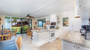 Una cocina amplia con una isla grande, muebles blancos y vistas a un jardín.