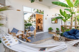 A hammock, a chair, and a blue bean bag chair in a room with a concrete floor and a large window.
