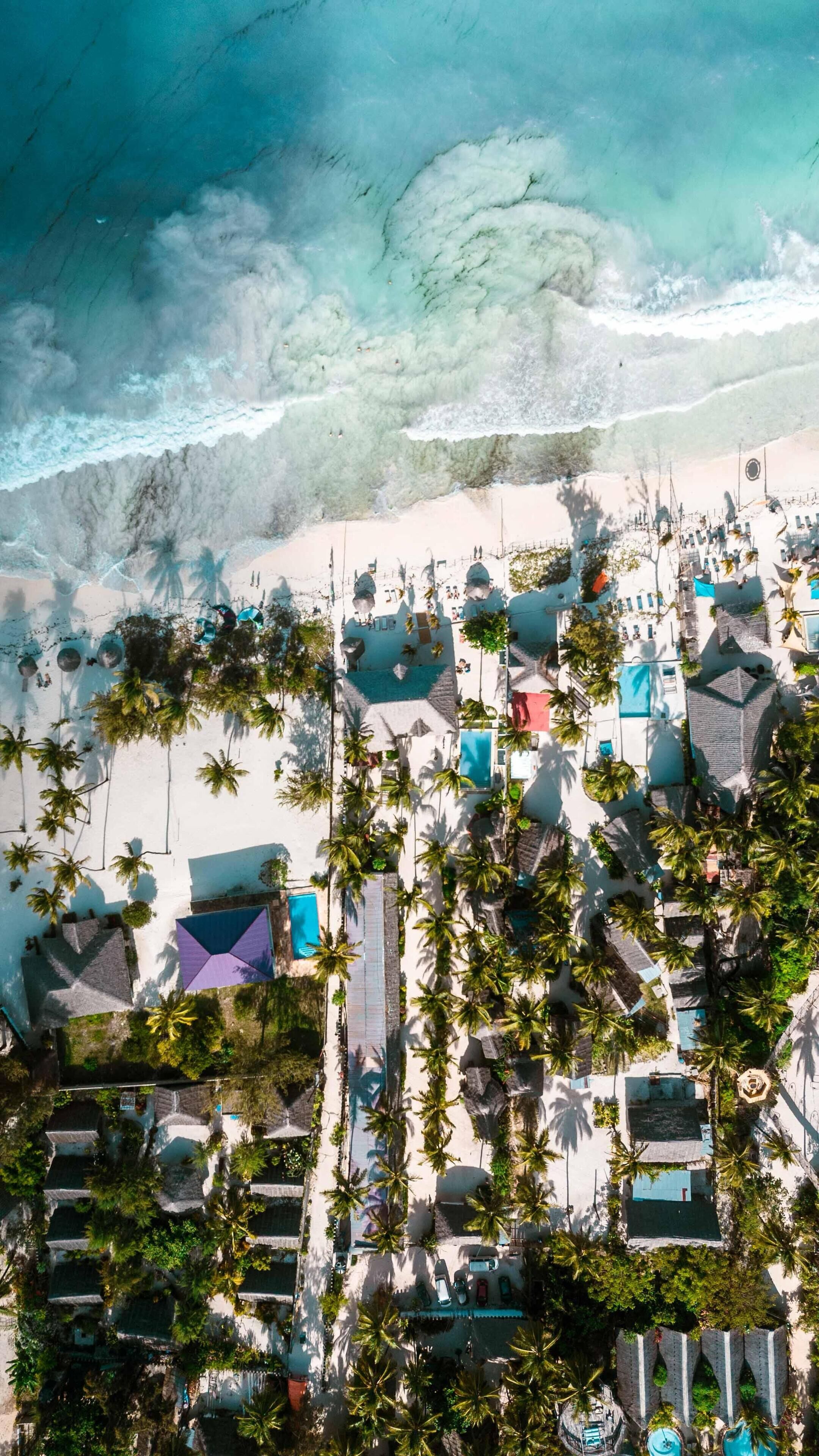 Vista aérea de un complejo turístico en la playa con varias cabañas tipo bungalow, un área de piscina central y una playa al fondo.