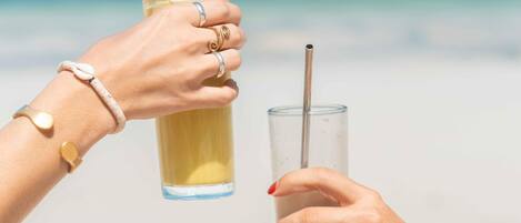 Dos manos sosteniendo vasos con pajitas en una playa.