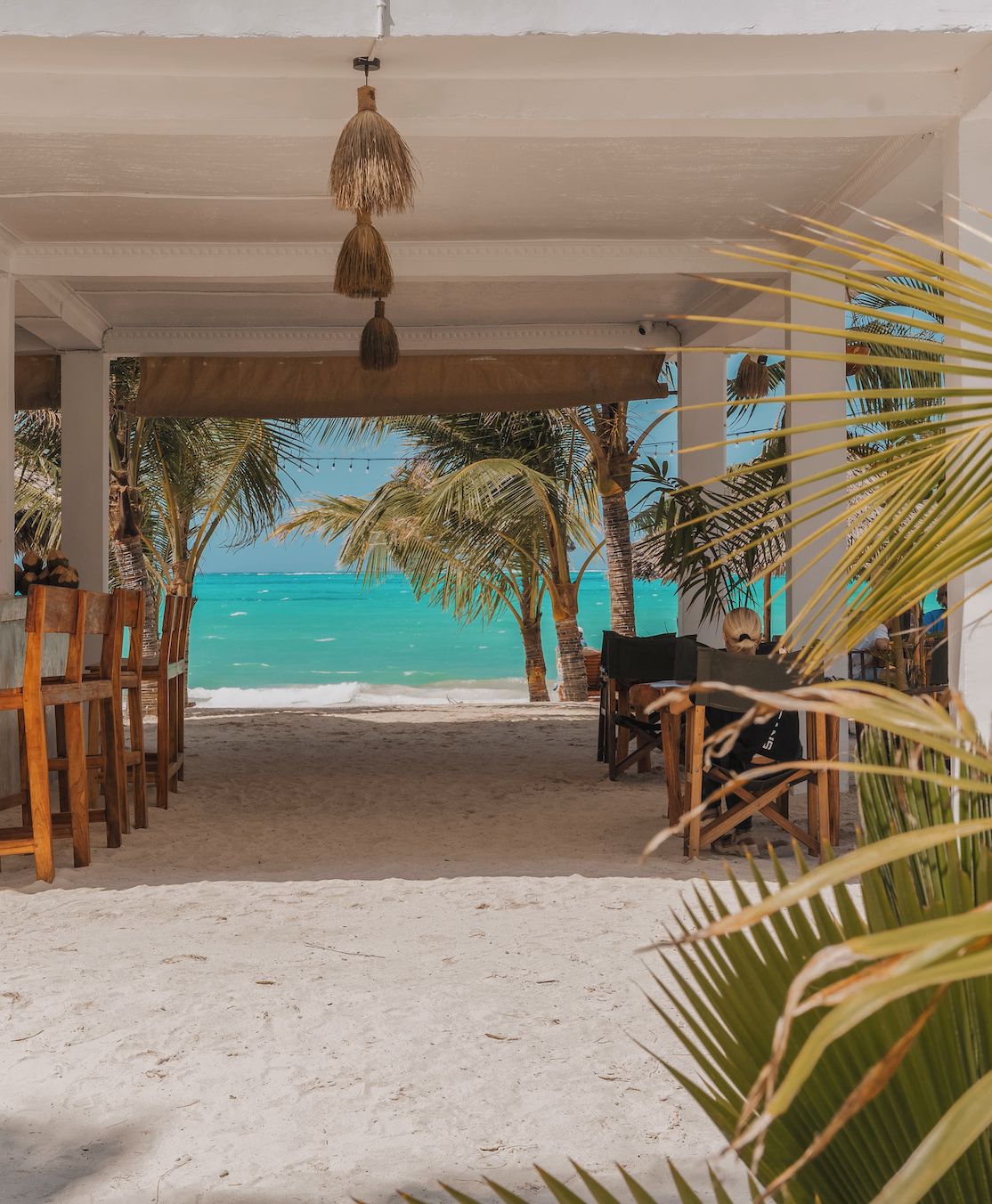 A beachside seating area with a view of the ocean, palm trees, and a hanging light fixture.