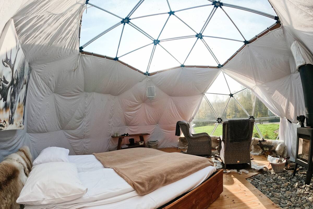 A cozy tented accommodation with a wooden bed, wicker chairs, and a view of the outdoors.