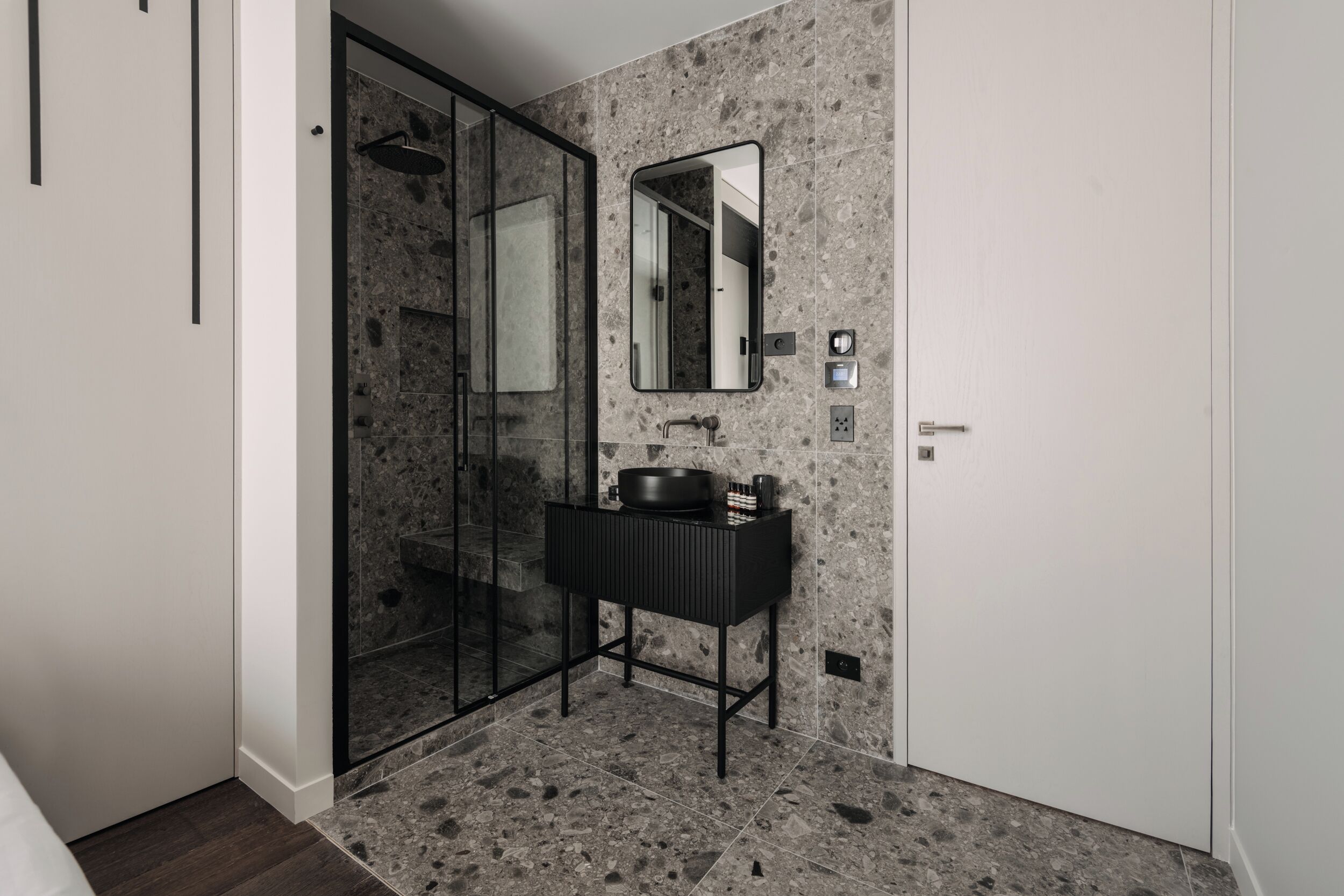 A modern bathroom with a glass shower enclosure, a black vanity, and a marble-tiled floor.