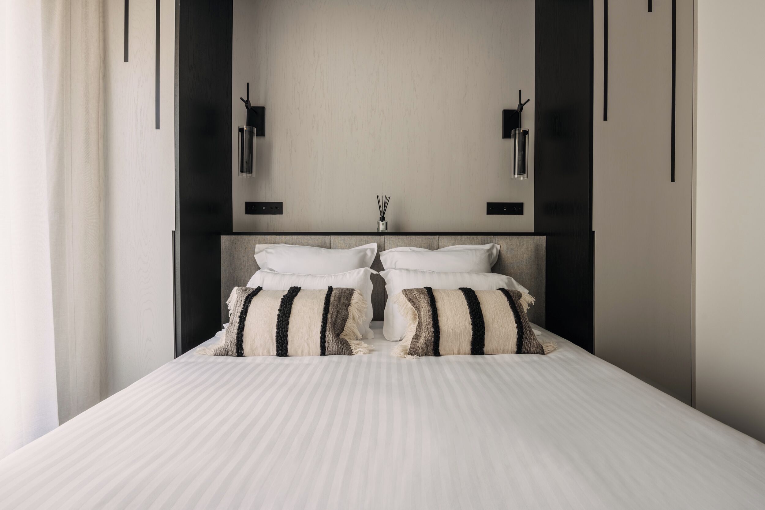 A modern bedroom with a large bed, two bedside tables, and a wall-mounted light fixture.