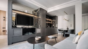 A modern living room with a large flat-screen TV, a sofa, a coffee table, and a dining area with chairs.