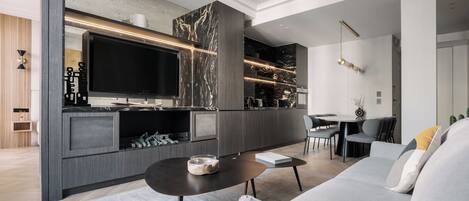 Una sala de estar moderna con un televisor de pantalla plana grande, un sofá, una mesa de centro y una zona de comedor con sillas.