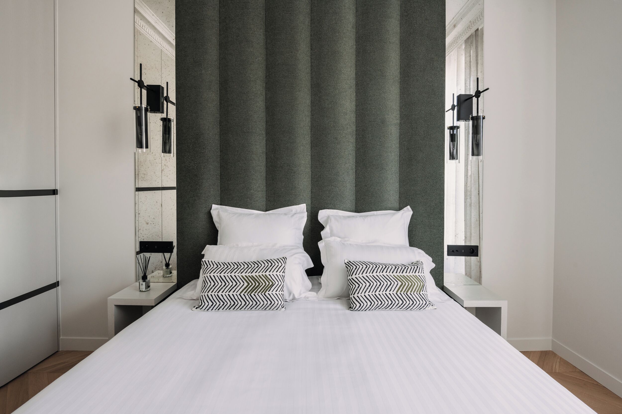 Un dormitorio moderno con una cama grande, dos mesitas de noche, un espejo y una pared de acento verde.