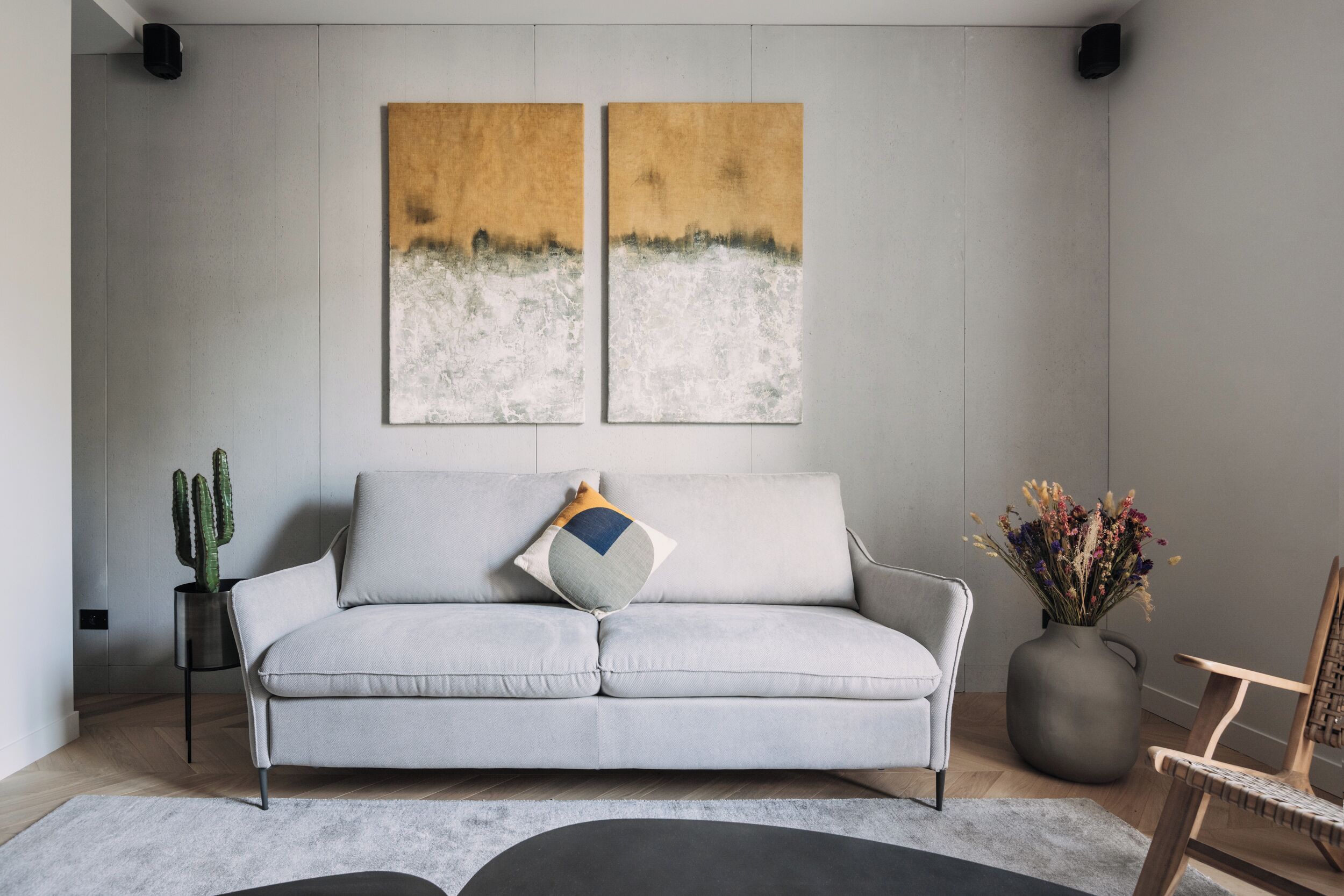 Ein modernes Wohnzimmer mit einem grauen Sofa, einer Kakteenpflanze, einer Vase mit Blumen und zwei abstrakten Bildern an der Wand.