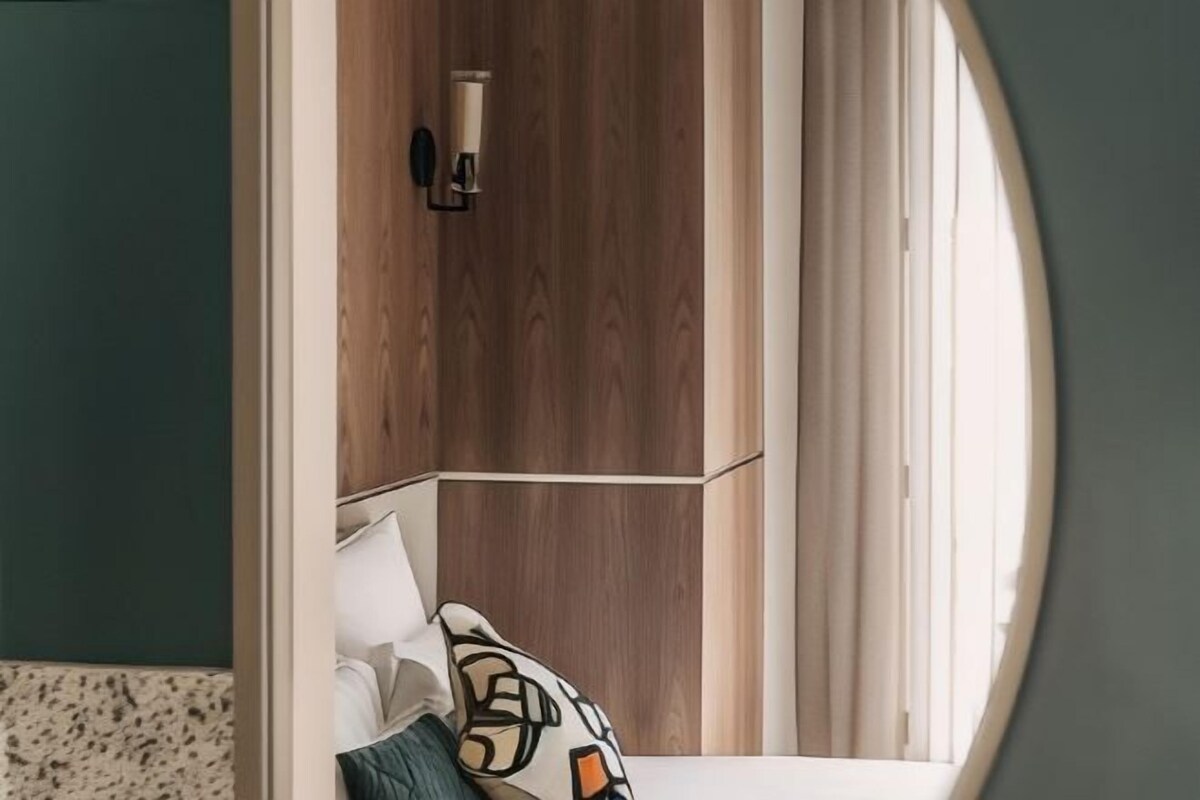 Quarto de hotel com parede de destaque em madeira, cama com roupa de cama branca e janela com cortinas.