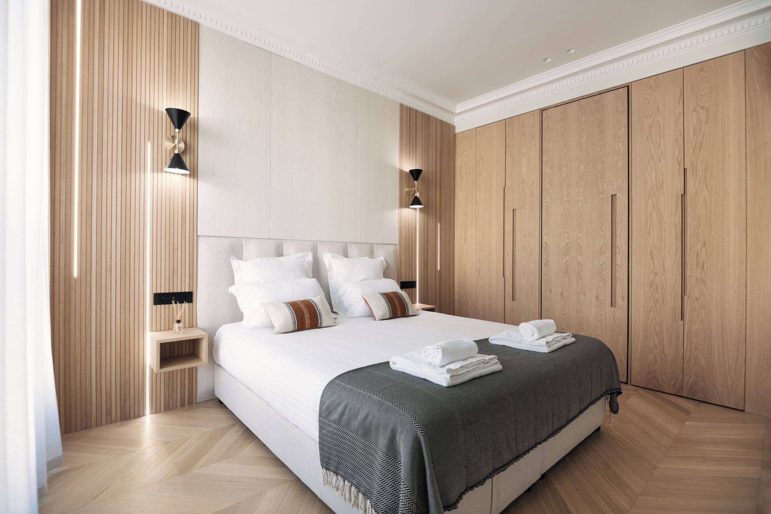 A modern bedroom with a large bed, wooden wardrobe, and bedside tables.