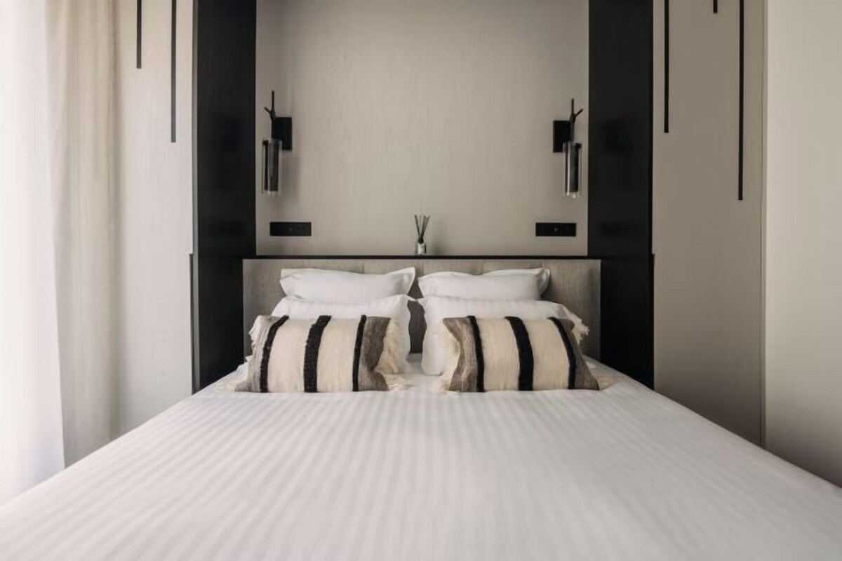 Quarto moderno com uma cama grande, duas mesas de cabeceira e uma luminária fixada na parede.