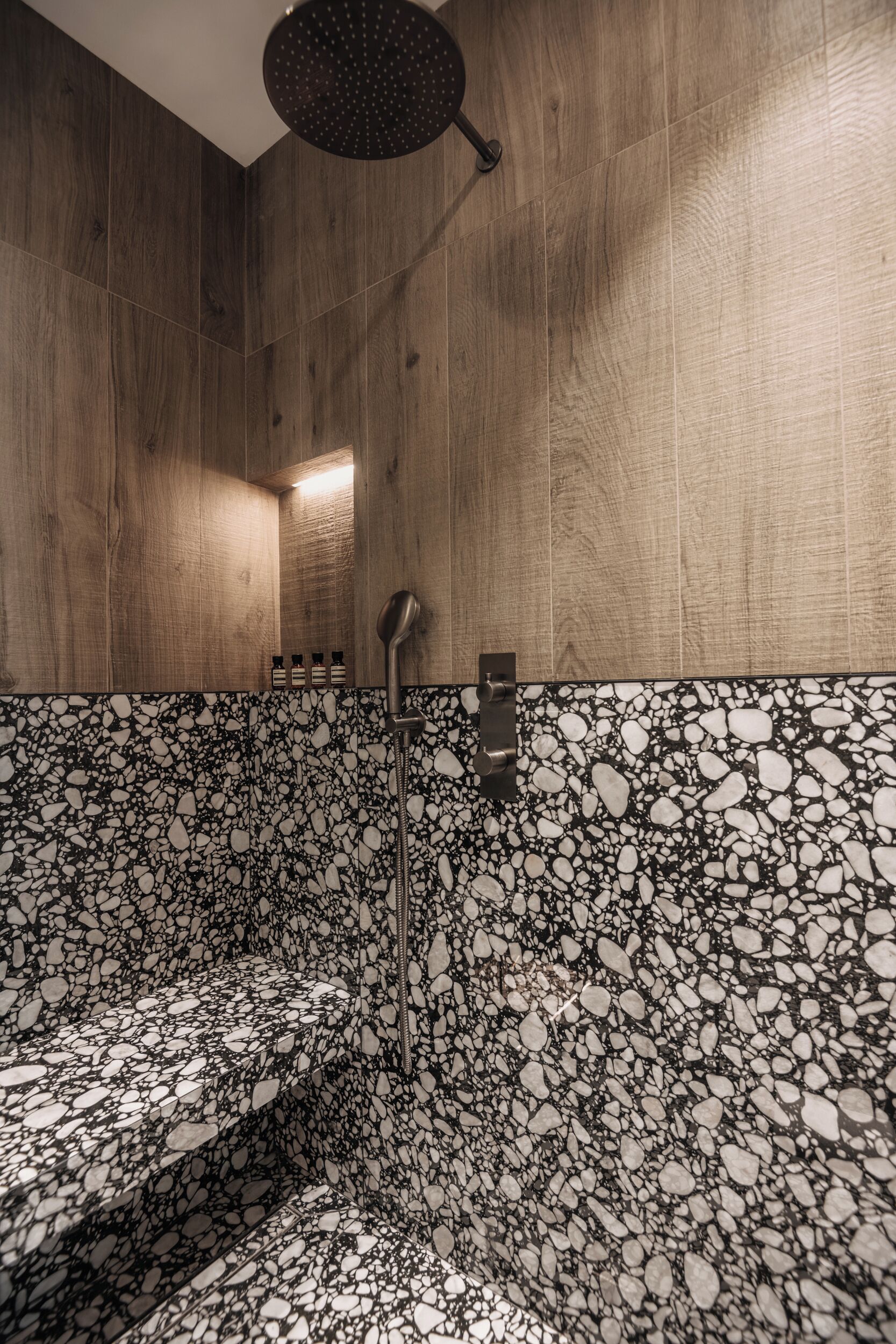 Een moderne badkamer met houten wanden, een vloer met een kiezenteffect en een douchekop.