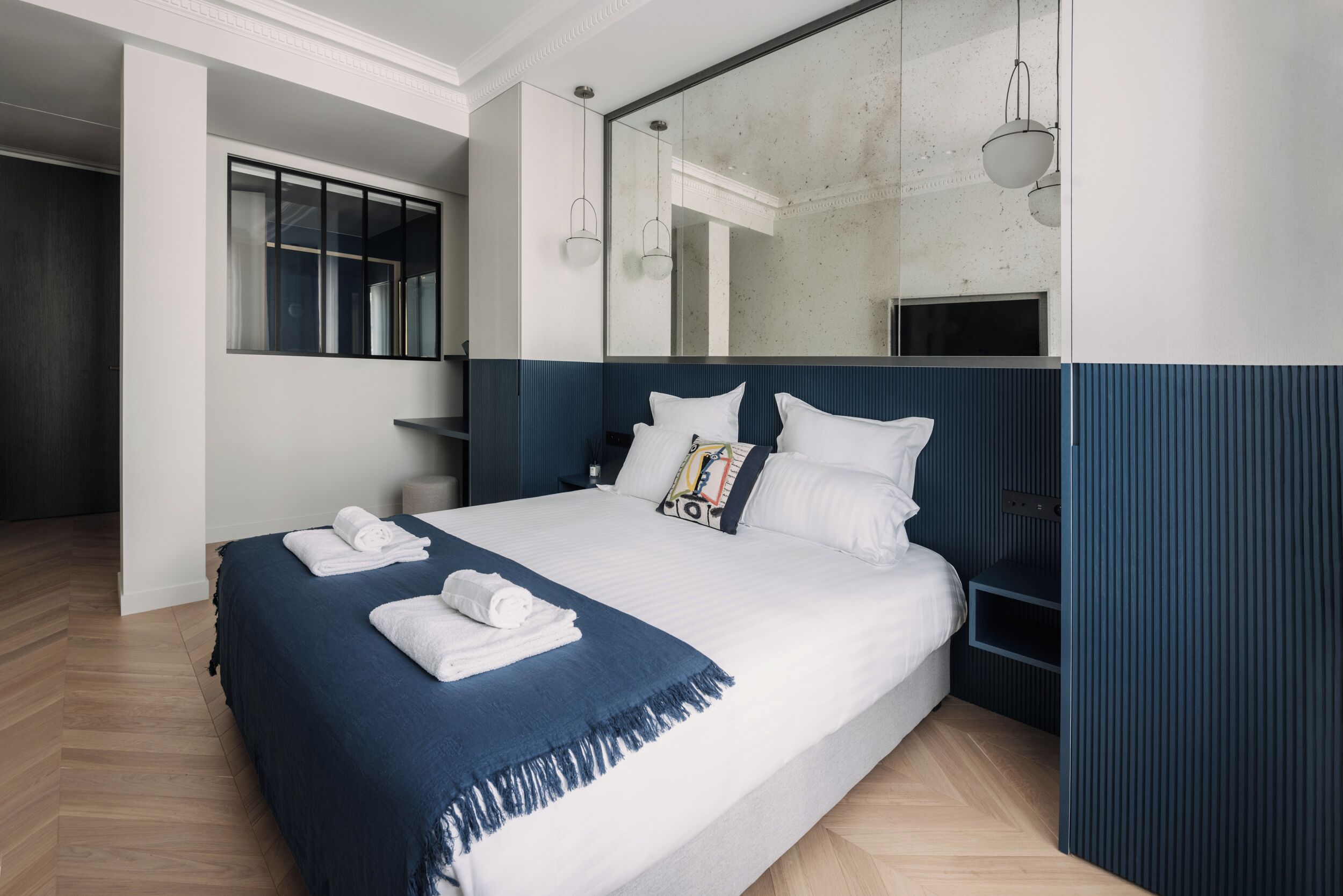 A modern hotel room with a large bed, a bedside table, a mirror, and a window.