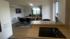 Eine moderne Küche mit integriertem Herd, einem Essbereich mit Tisch und Stühlen sowie einem großen Fenster mit Vorhängen.