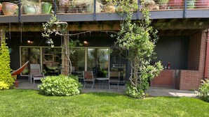 Une terrasse extérieure moderne, dotée d’une véranda en verre, d’un espace salon et de plantes en pot.