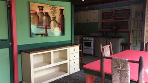 A room with a green wall, a painting of vases, a white cabinet, a red table, and a wicker chair. - Creole Style two bed 34 (Gros Islet)
