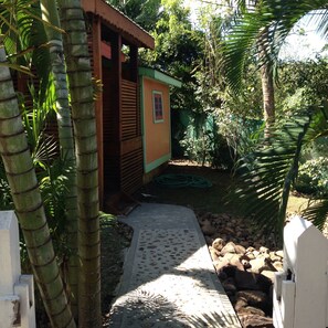 A pathway leading to a small wooden structure with a door, surrounded by lush greenery and rocks. - Creole Style two bed 34 (Gros Islet)