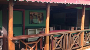 A wooden deck with a red table and chairs, a green wall with a painting, and a kitchen area in the background. - Creole Style two bed 34 (Gros Islet)