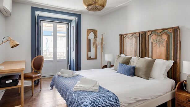 A bedroom with a large bed, a desk, a chair, and a wardrobe. - Master Deco Gem in Baixa (Lisboa)