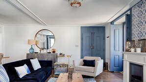 A living room with a dark blue sofa, a white armchair, a wooden coffee table, and a blue door in the background. - Master Deco Gem in Baixa (Lisboa)