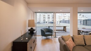 A modern living room with a sofa, a chair, a table, and a lamp. There is a large window offering a view of buildings outside. - Master Deco Gem in Cascais (Cascais)