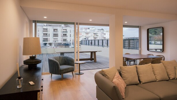 A modern living room with a sofa, a table, and a chair. There is a balcony with a railing and a view of buildings. - Master Deco Gem in Cascais (Cascais)