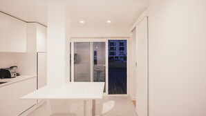 A compact kitchen with a white table and chairs, a refrigerator, and a sliding glass door leading to an outdoor area. - Master Deco Gem in Cascais (Cascais)