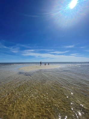 A beach with clear shallow waters, a sandy shore, and a clear sky.