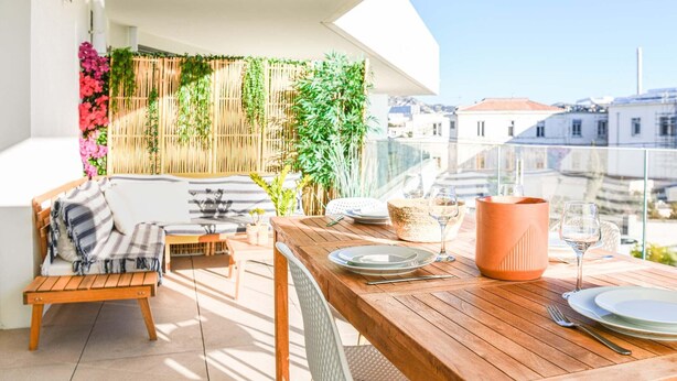 A balcony with a wooden table set for dining, a cushioned chair, and a sofa. - Bail mobilité - Appart 2 ch parking et terrasse (Marseille)