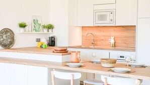 A modern kitchen with white cabinets, a wooden countertop, a built-in microwave, and a sink. There are plants on the countertop and a welcome box. - Bail mobilité - Appart 2 ch parking et terrasse (Marseille)