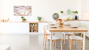 A modern kitchen with white cabinetry, a wooden dining table, and white chairs. There are potted plants on the counter and a decorative plate on the wall. - Bail mobilité - Appart 2 ch parking et terrasse (Marseille)