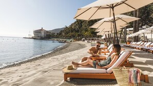 A beachside lounge area with sun loungers and umbrellas, a clear view of the sea, and a building in the background. - Remodeled 2BR -Prime Location -Private Views Patio (Avalon)
