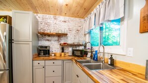 Een keuken met een bakstenen muur, houten kasten, een roestvrijstalen koelkast, een magnetron en een spoelbak.