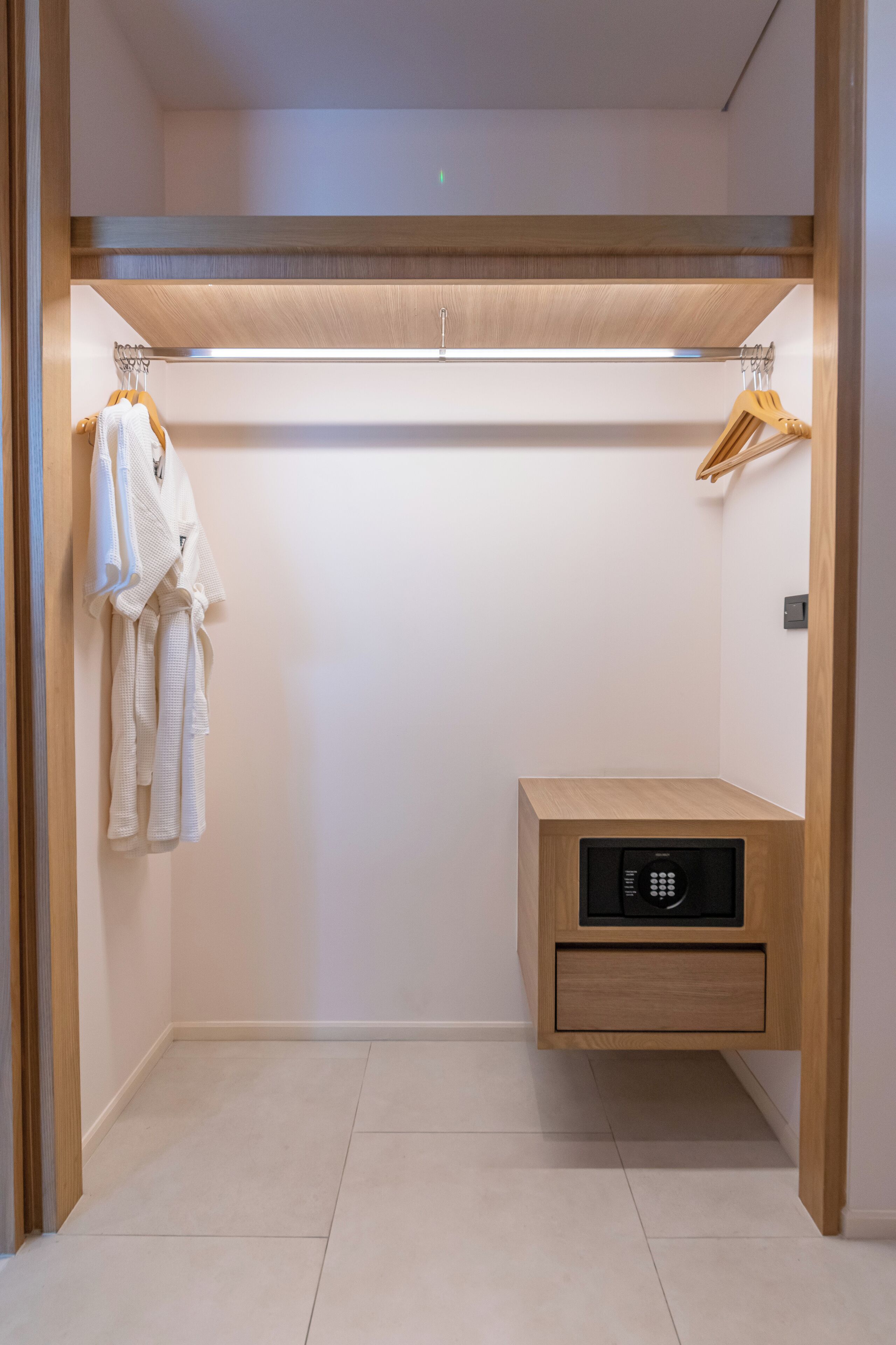 A walk-in closet with hanging robes, a wooden cabinet, and a built-in safe.