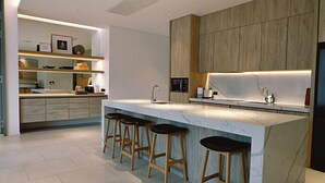 A modern kitchen with a marble countertop, wooden cabinets, and bar stools. - Villa De Time The Luxury Private Pool Villa (Pattaya)