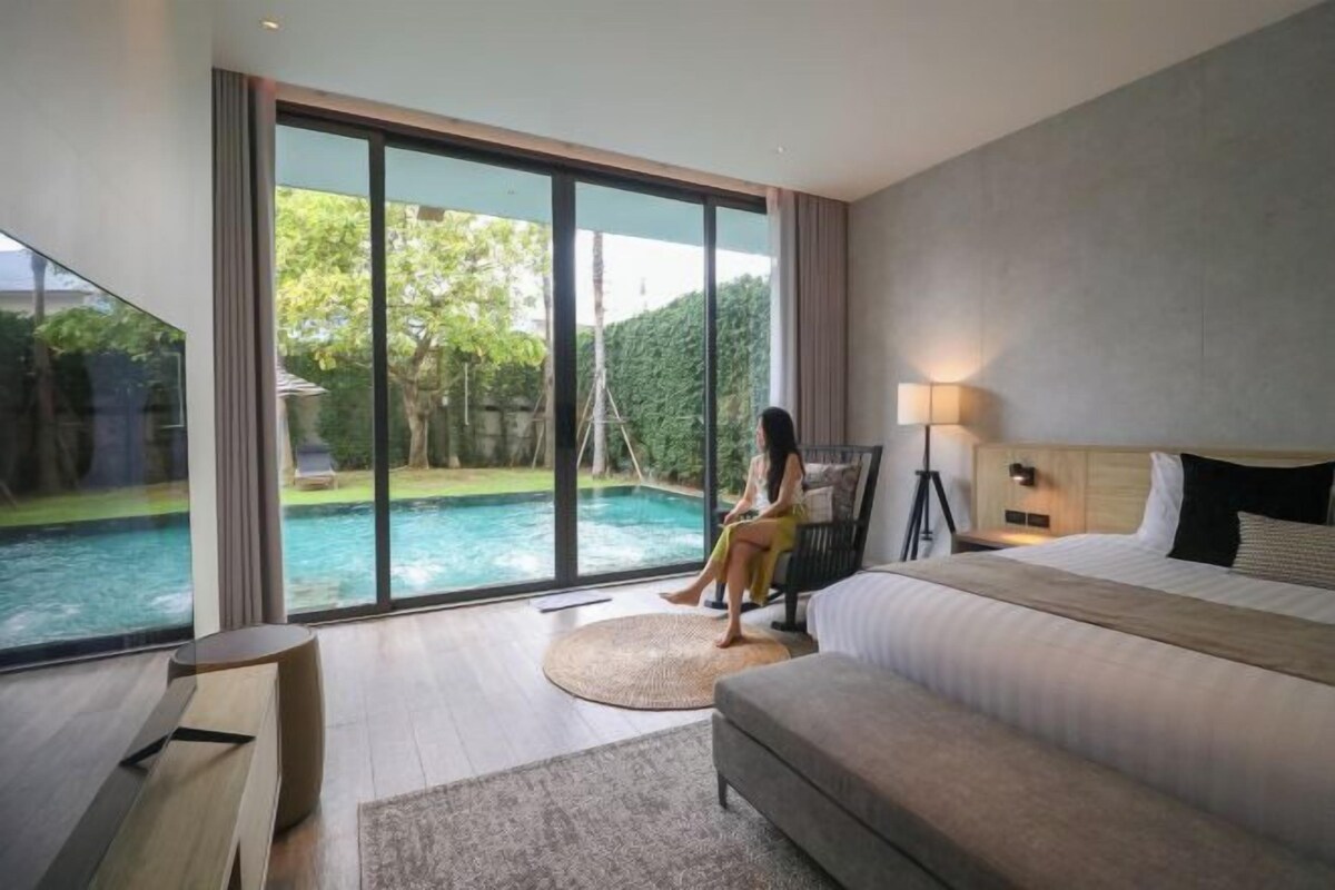A modern hotel room with a large bed, a desk, and a view of a swimming pool.