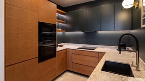 A modern kitchen with wooden cabinets, a black oven, a stainless steel sink, and a countertop with a built-in microwave.