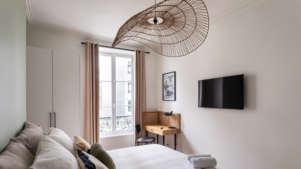 A hotel room with a bed, a desk, a chair, a television, and a window with curtains.