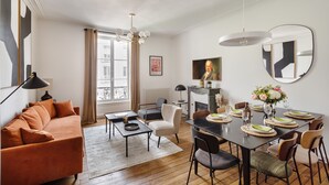 A modern living room with a sofa, dining table set for six, and a fireplace.