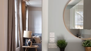 Ein modernes Wohnzimmer mit Holzboden, einem runden Spiegel, einem kleinen Hocker, einer Lampe und einem Blumentopf.