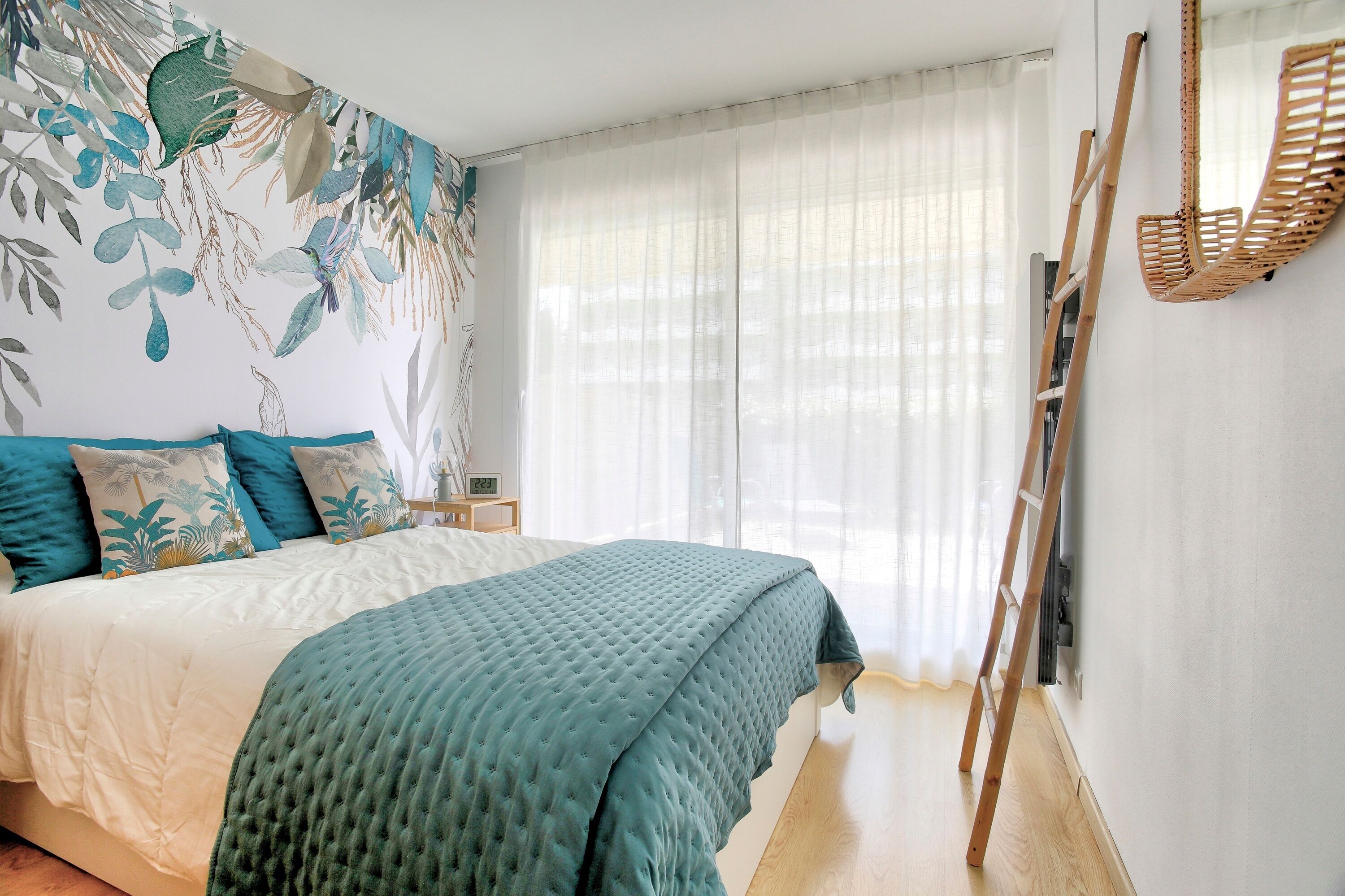 Een slaapkamer met een bed, een ladder en een muur met een bladpatroon.