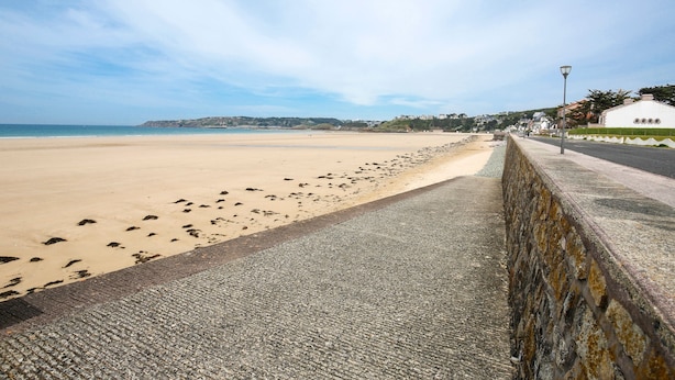 A coastal walkway with a sandy beach, a stone wall, and a building with a white facade.